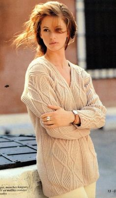 a woman is posing with her arms crossed and looking at the camera while wearing a sweater