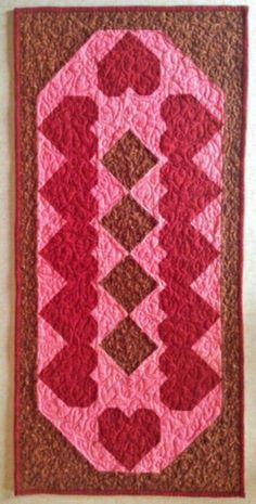 a pink and brown quilt hanging on the wall next to a white wall with a red border