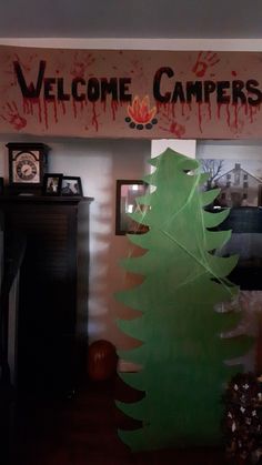 a welcome camper sign hanging from the ceiling above a green christmas tree in front of a fireplace