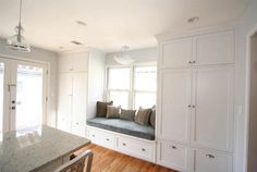 a kitchen with white cabinets and a window seat in the center, along with a marble counter top