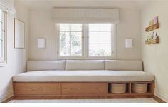 a white couch sitting under a window next to a wooden shelf on top of a hard wood floor