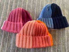 three knitted hats sitting on top of a bed next to each other in different colors