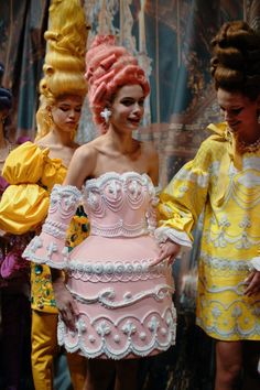 three women dressed in costumes and wigs standing next to each other with one woman's face painted pink