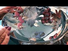 two hands reaching for leaves in a glass bowl filled with water and other things on the table