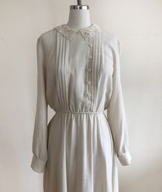 "Long-sleeved, ivory dress with pintucks and embroidered lace collar, from the 1980s. Bust measures 19\" (48.5 cm) flat across and waist measures 12-17.5\" (30.5-44.5 cm) flat across. The dress is 45\" (114 cm) in length. Original size is an 11. Cotton blend." Cream Long Sleeve Dress With Lace Collar, Classic Long Sleeve Dress With Lace Collar, Feminine Vintage Cream Dress With Lace Trim, Fitted Vintage Dress With Lace Collar For Daywear, Classic Lined Vintage Dress For Daywear, Classic Vintage Dress For Daywear, Lined, Beige Long Sleeve Vintage Dress For Formal Occasions, Cream Long Sleeve Vintage Dress, Spring Cream Dress With Peter Pan Collar