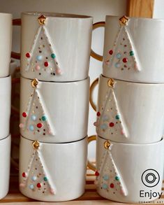 white cups with christmas trees on them stacked next to each other in front of a wooden shelf