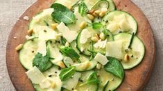 a pizza with cucumbers, pine nuts and mint leaves on it sitting on a wooden platter