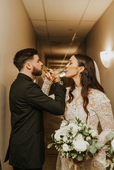 a bride and groom are drinking champagne together in the hallway at their wedding reception venue