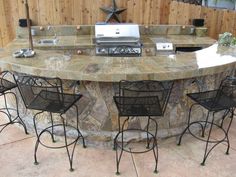 an outdoor kitchen with grill and bar stools around the island in front of it