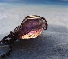 Stunning double terminated Phantom Amethyst Crystal from the Mwana Lubaba Mine in Zambia is a rare stone combining smoky quartz and amethyst. The crystal formation has rich interior patterns with red hematite inclusions. Formed over millions of years sustaining changes in molten temperatures and tectonic movement within the earth, this crystal is in its natural rough form, not cut or polished in any way.  The crystal  is simply wire wrapped and strung on an oxidized copper ball chain 27" long. (Note: prop does not show true length of chain) Stone size is  1 1/8" long and 5/8' at the widest point.  Phantom crystals are named for the crystal formations which float from within the stone giving it a double crystal appearance.  Note: oxidized metal finishes are more sensitive to salt water, per Large Purple Stone Crystal As Gift, Large Purple Spiritual Stone Crystals, Large Purple Stone Crystals As Gift, Purple Crystals With Large Stone As Gift, Spiritual Large Purple Stone Crystals, Spiritual Amethyst Crystal For Gift, Spiritual Large Purple Crystals, Handmade Amethyst Crystals For Meditation, Handmade Amber Jewelry With Amethyst