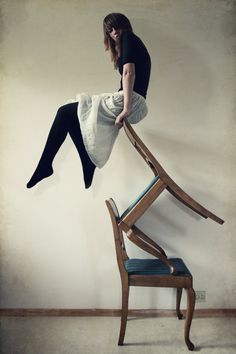 a woman sitting on top of a wooden chair with her legs up in the air