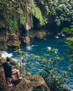 a man sitting on top of a cliff next to a river in the jungles