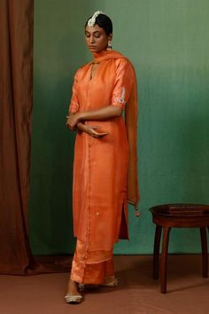 Rust orange silk kurta with placement vintage motif, contrast thread, zari, bead and sequin embroidered half sleeves. Paired with tissue stripe pattern straight pant and organza embroidered dupatta.
Components: 3
Pattern: Embroidered
Type Of Work: Sequin, Zari, Thread and Bead Work
Neckline: V Neck
Sleeve Type: Half Sleeves
Fabric: Kurta: Silk, Pant: Tissue, Dupatta: Organza
Color: Orange
Other Details: 
Tasselled dupatta edges
Beaded hem details
Lace work dupatta border
Side slits on kurta
Occa Orange Raw Silk Sets With Zari Work, Orange Zari Work Art Silk Sets, Orange Art Silk Sets With Zari Work, Orange Raw Silk Saree Set, Orange Raw Silk Set With Dupatta, Orange Silk Sets With Resham Embroidery, Designer Orange Raw Silk Kurta, Semi-stitched Orange Raw Silk Kurta, Orange Raw Silk Kurta For Designer Wear