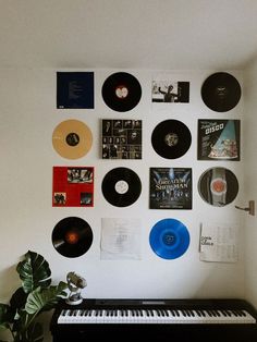 there are many records on the wall and a piano in front of it with a potted plant next to it