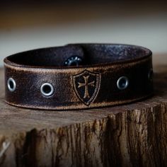 Made from premium grade 7 ounce leather. Comes engraved with the Crusader cross and shield shown centered between gunmetal eyelets. Strap is .75 inches wide. Hand dyed, distressed, oiled and finished in house. Made in America. Please note that adding personalization will replace the engraving shown. Instructions can be added in the note at checkout. Rustic Leather Concho Bracelets, Vintage Leather Bracelet With Engraving, Vintage Leather Concho Bracelets, Vintage Stamped Leather Cuff Bracelet, Stamped Leather Vintage Cuff Bracelet, Vintage Engraved Leather Bracelets, Vintage Leather Engraved Bracelet, Brown Engraved Leather Bracelet, Engraved Brown Leather Bracelet