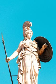 an image of a statue holding a shield and spear on top of a building with a blue sky in the background