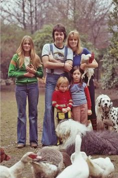 a group of people standing next to each other in a field with dogs and chickens