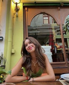 a woman sitting at a table in front of a store window smiling for the camera