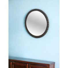 a round mirror hanging on the wall above a wooden dresser in a blue walled room