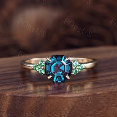 an image of a ring with blue and green stones on it sitting on a wooden surface