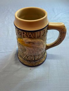 a ceramic mug with an eagle painted on the front and sides, sitting on a white tablecloth