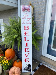 a sign that says believe on it next to some pumpkins and flowers in front of a house