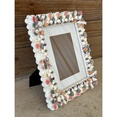 a white frame with seashells and pearls on it sitting next to a wooden wall