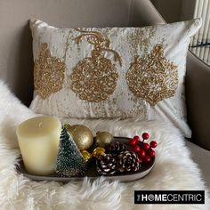 a tray with christmas decorations and a candle sitting on a chair next to a pillow