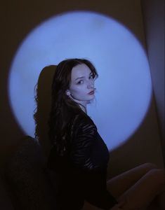 a woman sitting in front of a white circle with blue light coming from behind her