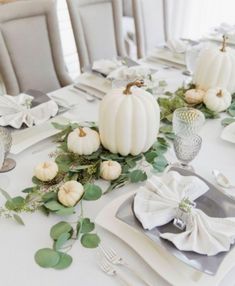 the table is set with white pumpkins and greenery