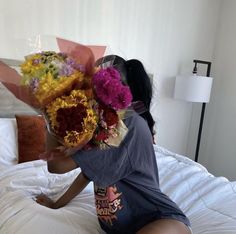 a woman sitting on top of a bed with flowers in her hair and holding onto the pillow