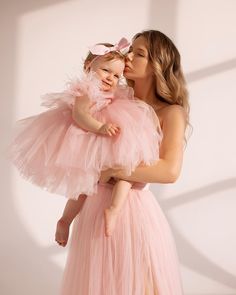 a woman in a pink dress holding a baby wearing a tulle skirt and matching headband