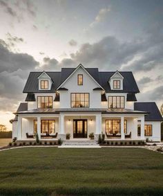 a large white house with lots of windows and grass in the front yard at sunset