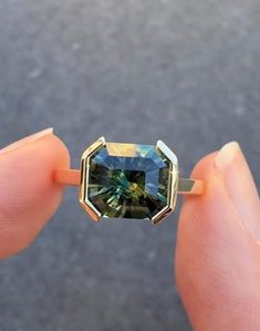 someone is holding a ring with a blue and green stone in it's middle