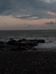 a person standing on rocks near the ocean under a cloudy sky with waves coming in