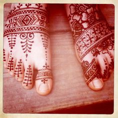 two feet with henna tattoos on them sitting on a wooden table next to each other