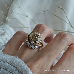 a woman's hand with a ring on it and flowers in the back ground