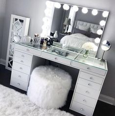 a white vanity with lights on it and a stool in front of the mirror that is next to it