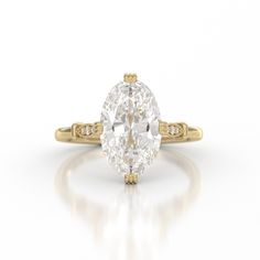 an oval cut diamond ring with yellow gold accents on the shoulders and sides, set against a white background