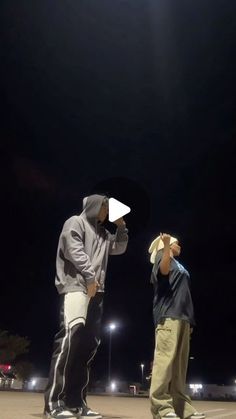 two young men standing next to each other on top of a parking lot at night