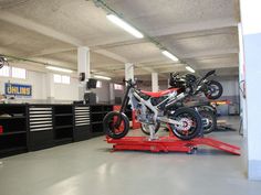 two motorcycles are parked in a garage with tools on the floor and one motorcycle is being worked on