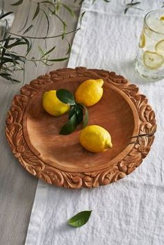 three lemons on a wooden plate with green leaves and water in the glass vase