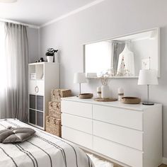 a bedroom with a bed, dresser and mirror on the wall next to it's windows