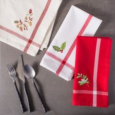 three red and white napkins with holly applique on them next to silverware