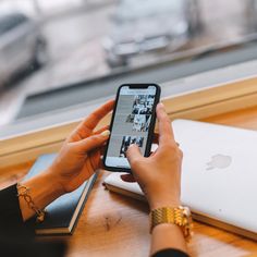 a woman is looking at her cell phone while sitting in front of an apple laptop