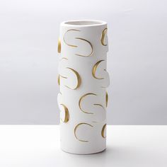 a tall white vase with gold circles on the outside and inside, sitting on a table