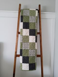 a green and white quilt hanging from a wooden ladder in front of a white wall