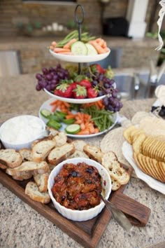 a table topped with plates of food next to crackers and fruit on top of a wooden cutting board