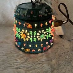 a green container with colorful lights on it sitting on a fur covered floor next to scissors