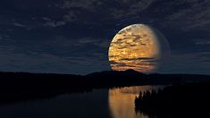 a full moon is seen over a lake in the middle of the night with trees around it